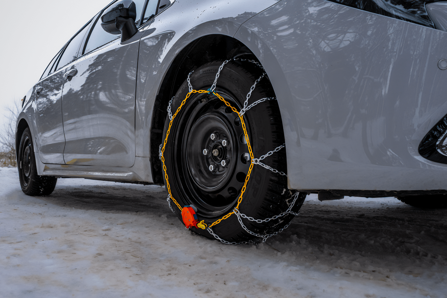 Widok od boku na oponę białego samochodu z założonym żółtym łańcuchem śniegowym z samonapinaczem