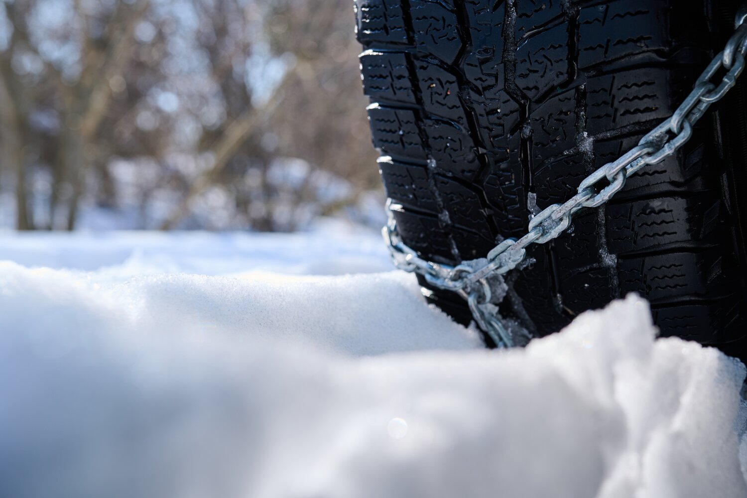 zbliżenie na oponę samochodową z zamontowanym łańcuchem. Widok od strony frontu bieżnika. W tle zaspy śniegu