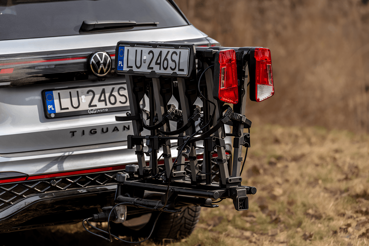Zbliżenie na tył srebrnego SUVa marki Volksvagen z zamontowaną na haku platformą rowerową. Platforma jest złożona i przyjęła formę walizki. Tablica rejestracyjna zamontowana jest na boku.
