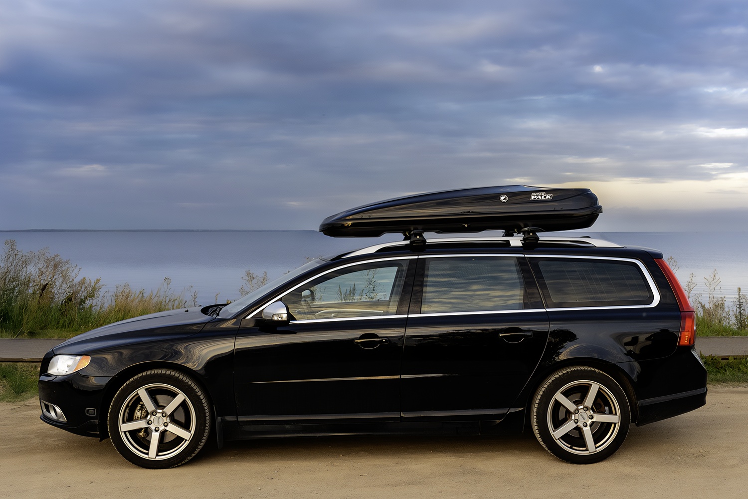 Widok od boku na czarne Volvo kombi z czarnym boxem dachowym zamontowanym na dachu. Na boxie logo z napisem 